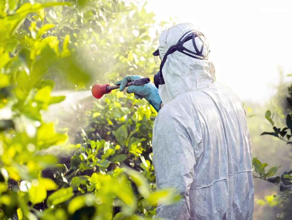 kmet v poplni opremi pri škropljenju s pesticidi